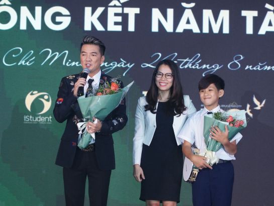 Bà Trần Thúy Trâm Quyên - Giám đốc Ban TT&TH tặng hoa cho ca sĩ Đàm Vĩnh Hưng và Hiếu Trung - phụ huynh và học sinh của trường SNA.